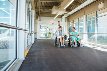 Medical Team Pushing Patients On Wheelchairs At Hospital Corrido