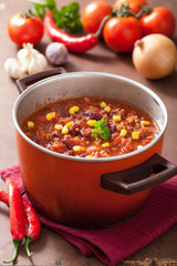 mexican chili con carne in red rustic pot with ingredients