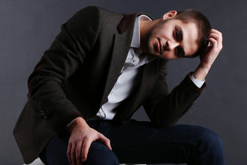 Handsome young sitting on cube on dark background