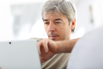 Mature man in sofa websurfing with tablet