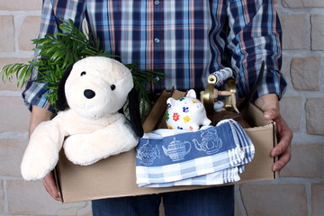 Mann trägt Umzugskarton mit Pflanze, Hund, Buch