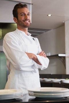 Happy young chef standing with arms crossed behind counter