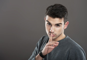 Portrait of a guy making a silence gesture, gray background