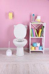 White toilet bowl and stand with books, on color wall