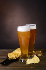 Glasses of beer with snack on table on dark background