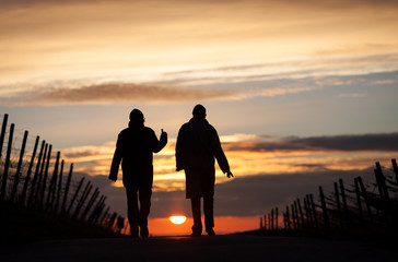 two silhouetted seniors walking in sunset - obrazy, fototapety, plakaty