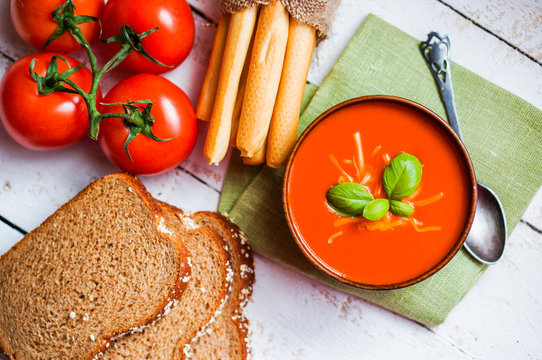 Tomatoe soup with bread sticks and basil on wooden background