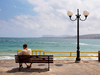 man sitting on a bench on the waterfront - obrazy, fototapety, plakaty