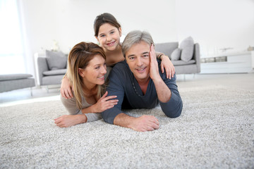 Middle-aged couple with little girl laying on carpet