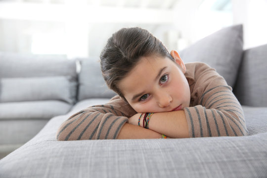 Portrait of sad little girl laying on couch