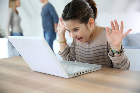 Young girl at home cwaving at laptop webcamera