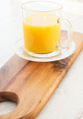 A cutting board wtih a mug of orange juice