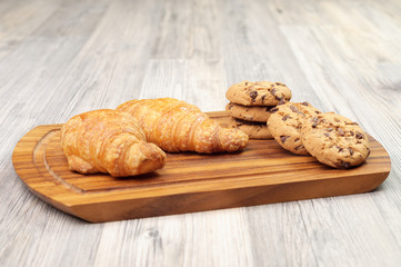 Croissants and chocolate chip cookies on a wooden board