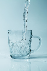 Water pouring into a clear cup on a gradient background