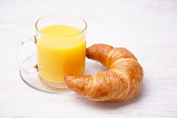 Orange juice in a glass cup and a french bun