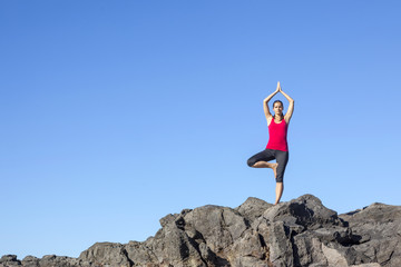 Young woman practicing tree yoga pose outdoor against blue sky