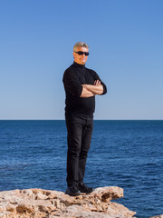 Mature businessman posing confident on a rock at the sea