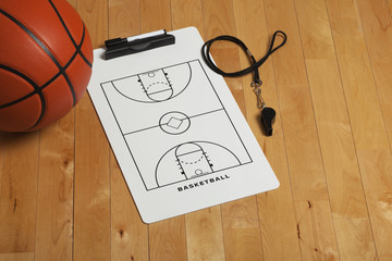 Naklejka premium Basketball with coach's clipboard and whistle on wooden floor