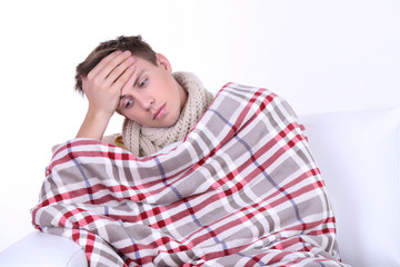 Guy wrapped in plaid sitting on sofa is ill