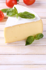 Tasty Camembert cheese with basil and tomatoes, on wooden table