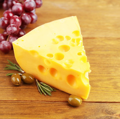 Piece of cheese with green olives, on wooden background