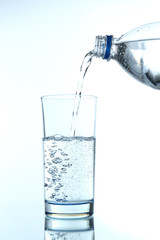 Pour water from bottle into  glass, on light blue background