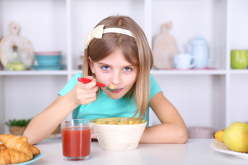 Beautiful little girl eating breakfast in kitchen at home