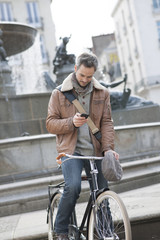 handsome man at phone on a bicycle with fountain in background