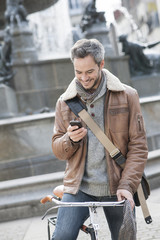 handsome man at phone on a bicycle with fountain in background