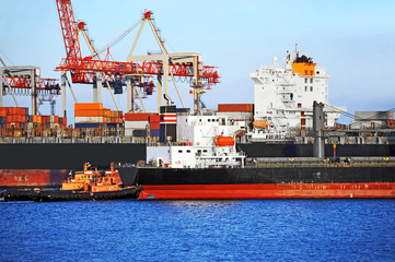 Tugboat assisting container cargo ship to harbor quayside