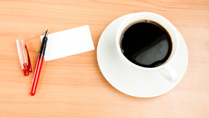 Top view of coffee cup, piece of paper and pen on the wooden tab