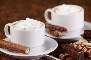 Two cups of coffee or hot cocoa with chocolates and  cookies on
