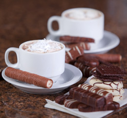 Two cups of coffee or hot cocoa with chocolates and  cookies on