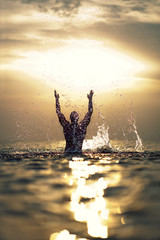Athletic man's silhouette with raised hands out of the sea with