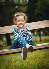 Cute little girl sitting on the bench in a park