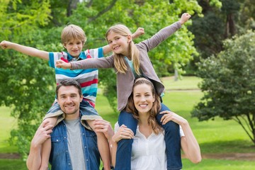 Fototapeta premium Happy parents carrying kids on shoulders at park