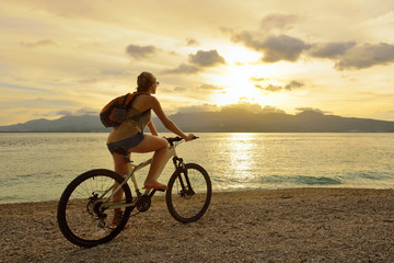 Obraz premium Young woman with backpack standing on the shore near his bike an