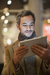 handsome man using a digital tablet outside with city lights at