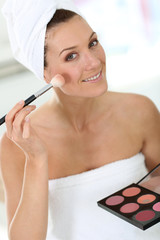 Smiling woman in bathroom applying makeup on