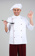 Professional chef in white uniform and hat, on gray background