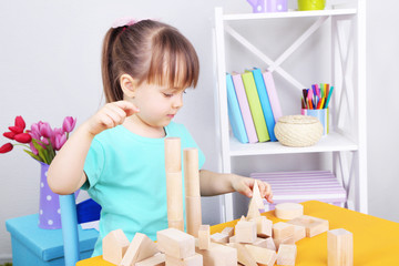 Little girl plays with construction blocks sitting at table in