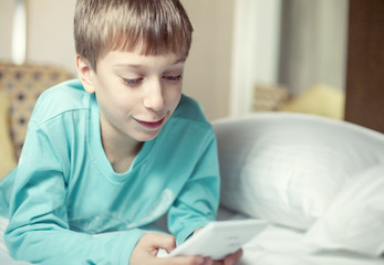 Beautiful child lying on a bed playing at computer toy smiling