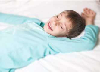 Lovely little boy peacefully sleeping in a bed smiling