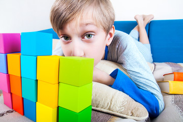 Cute funny child lying on a sofa playing with colorful cubes