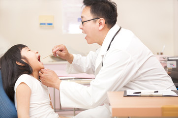 Obraz premium Little girl having throat examination with tongue depressor