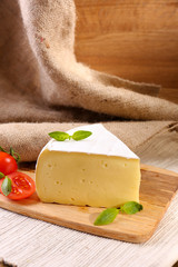 Tasty Camembert cheese with tomato and basil, on wooden table