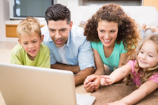 Cute siblings lying on the rug using laptop with their parents