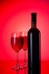 Glasses and bottles of red wine on red background
