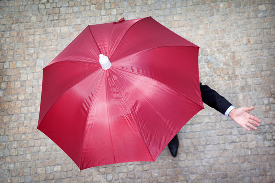Businessman hidden under umbrella and checking if it's raining