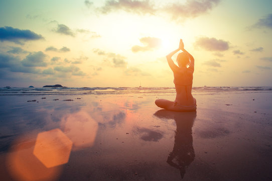 Silhouette young woman practicing yoga on the beach.